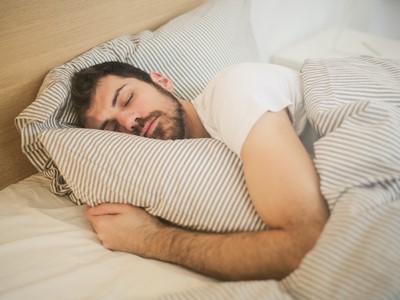 man sleeping in bed cuddling pillow - air conditioning helps sleep